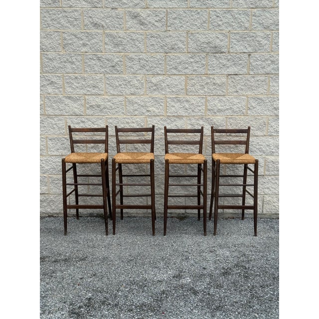 Set of four vintage wooden bar stools featuring slender frames, double-slat ladder backs, and handwoven natural rush seats.