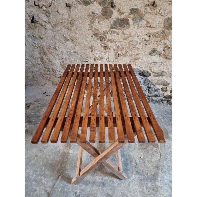 A mid-20th century folding table made of solid pine, characterised by its simple construction and practical design. The...