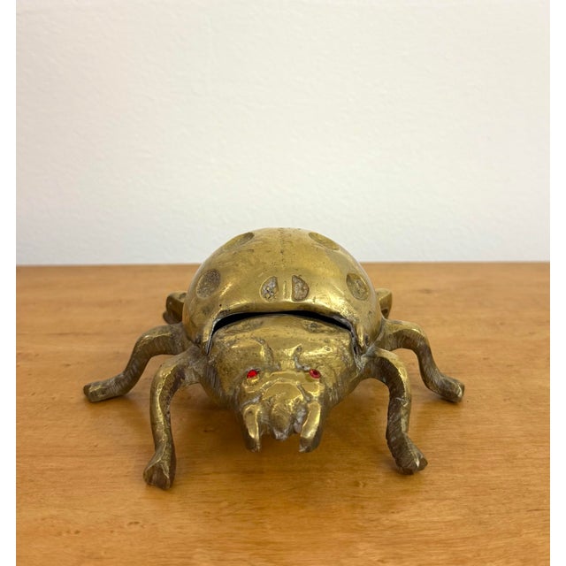 A whimsical brass ladybug featuring a domed, spotted shell, sculpted legs, and red jewel-like eyes. The hinged shell lifts...