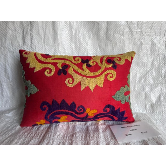 A beautifully hand-embroidered 1900s Suzani pillow featuring golden scroll motifs and deep violet floral accents on a rich...