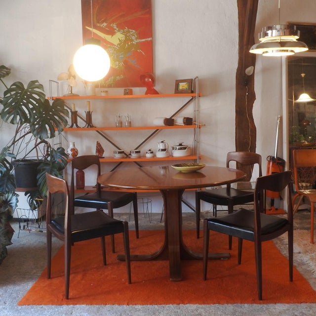 Table for four, crafted from walnut. The circular tabletop rests on a central pedestal that branches into four lower legs....