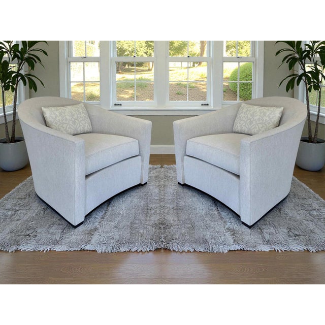 A pair of Holly Hunt Sevilla swivel lounge chairs. The comfortable barrel-style back is enhanced with the down-filled...