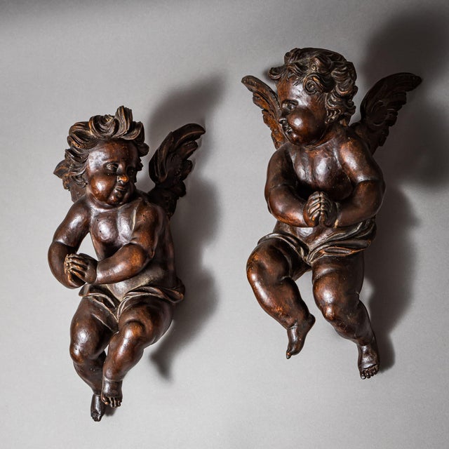 Pair of Baroque wall angels with wings, loincloths and curly hair. Their hands are folded in prayer. Carved wood with a...