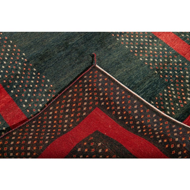 Beautiful modern Persian Gabbeh hand-knotted wool rug with a green field. This piece has a red frame in a gorgeous...
