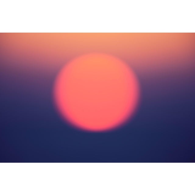 This photograph captures a softly blurred sunset, where the sun appears as a luminous orb against a gradient of warm hues...