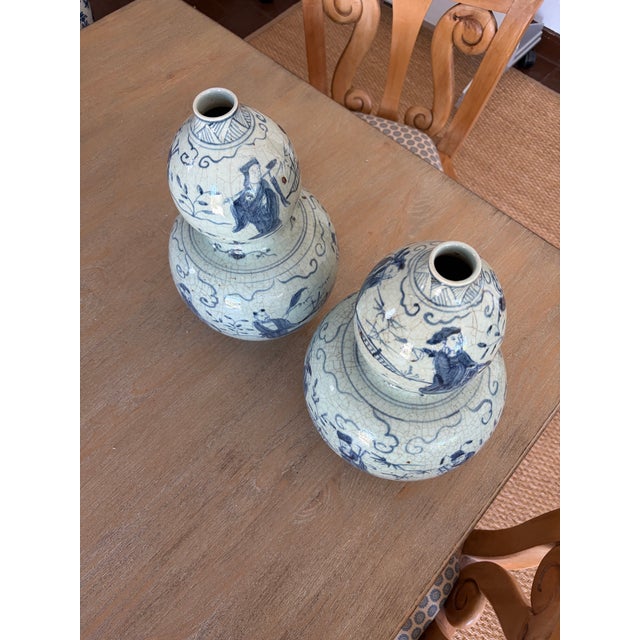 A striking pair of gourd-shaped vases, rendered in classic blue and white, features delicate Asian-inspired artwork that...