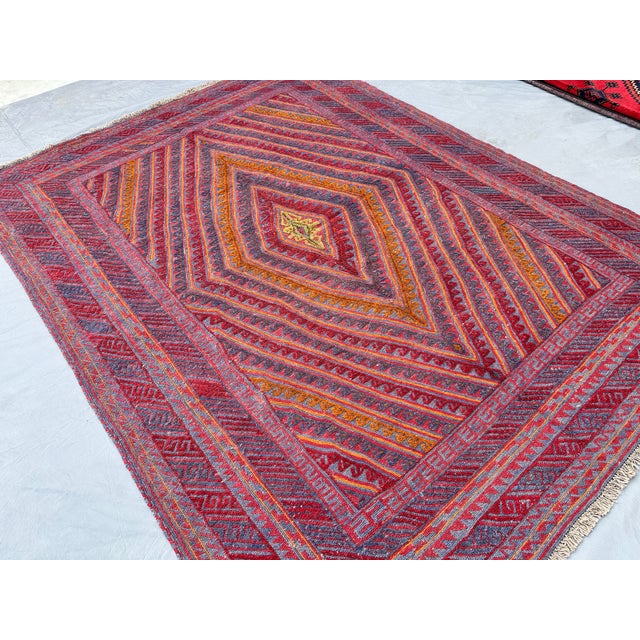 This bold Maimana kilim features a large concentric diamond medallion built from radiating zigzag bands in rich red,...