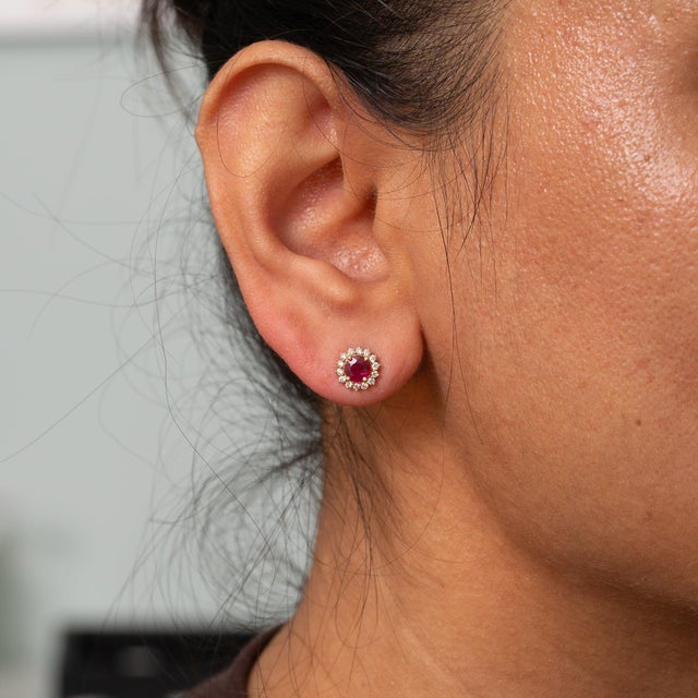 A matched pair of burma ruby stones, round cut, totalling 0.87 carats anchors these solid 14K yellow gold earrings, haloed...