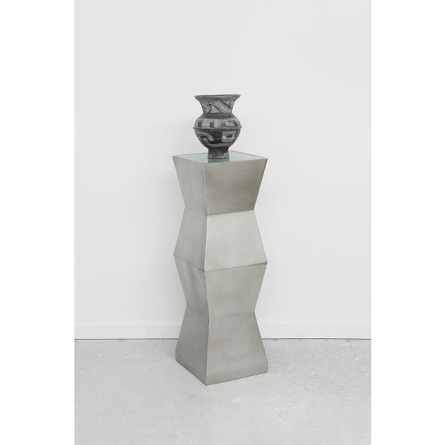 Vintage illuminated pedestal featuring a sculptural faceted silhouette in a brushed metal finish with a recessed glass...