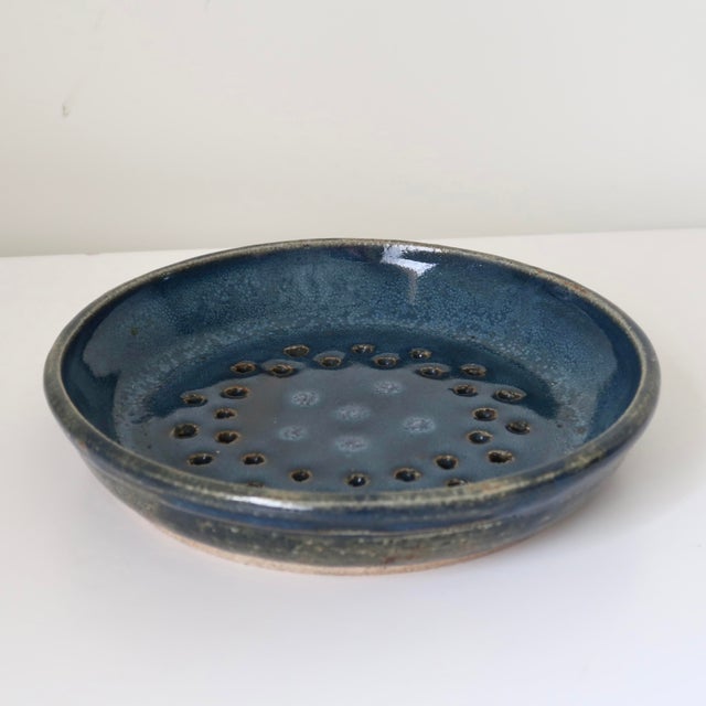 Signed handmade studio pottery draining dish or berry bowl featuring a rich mottled blue glaze with earthy undertones and...