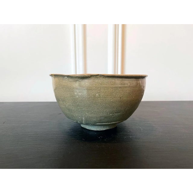 A ceramic bowl with celadon glaze from Korea, circa 14th century (late Goryeo Dynasty). The particular shape of the bowl...