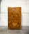 Vintage Lane armoire featuring a sculptural patchwork facade of raised geometric wood panels. A warm honey finish...