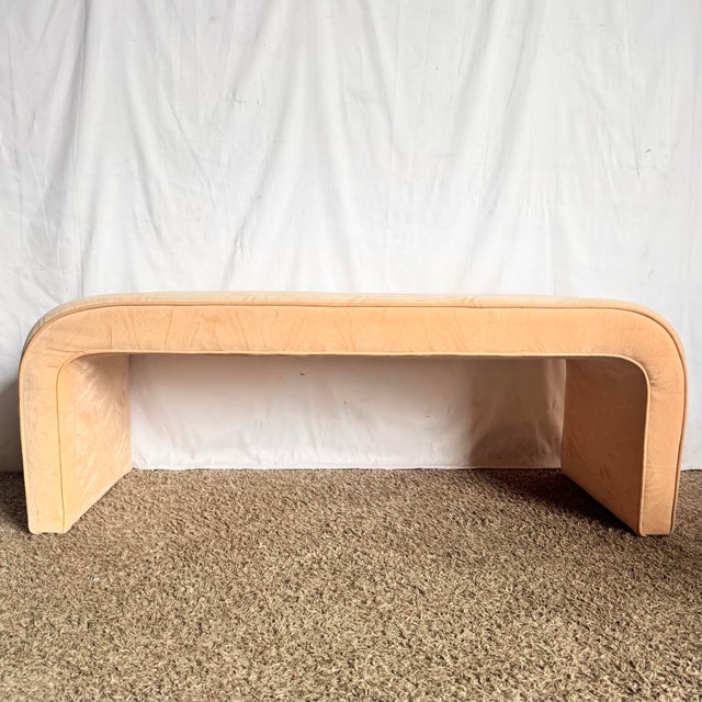 This sculptural postmodern waterfall bench features a softly curved silhouette upholstered in plush peach velvet fabric,...