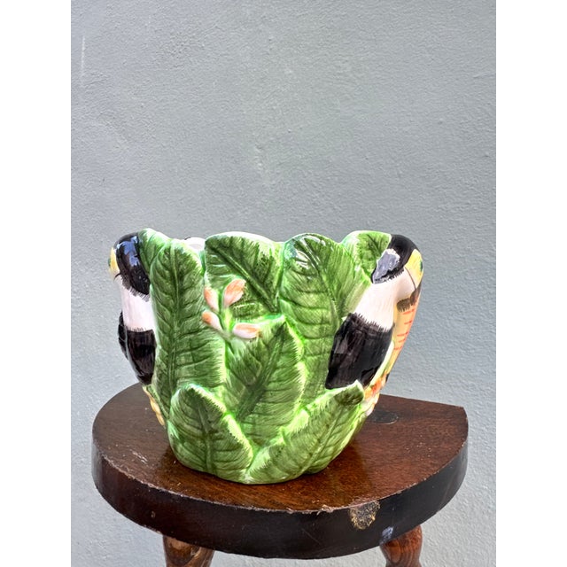 A joyful and boldly sculpted majolica bowl featuring a life-sized toucan emerging from a dense tropical leaf surround —...