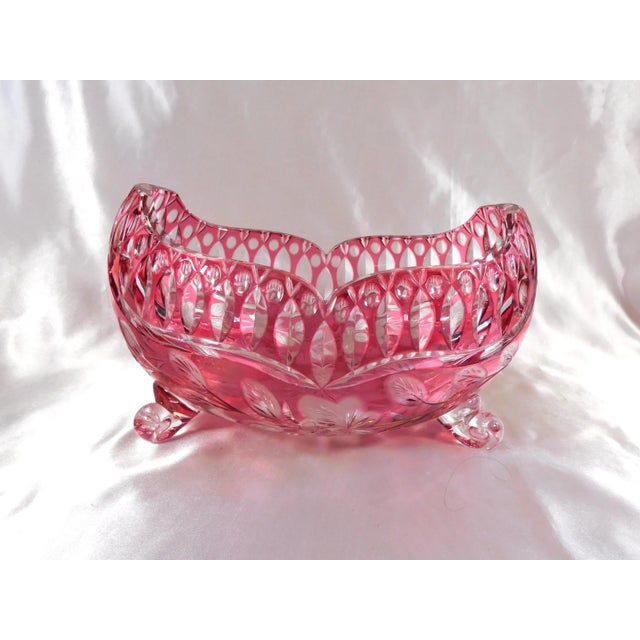 This is a large pink cut to clear bowl with four glass feet. The bowl has an all over cut design with a shaped edge. It...