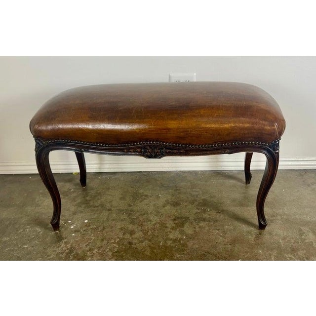 Elegant French Louis XV–style bench featuring a beautifully aged hand-finished leather seat and richly carved hardwood...