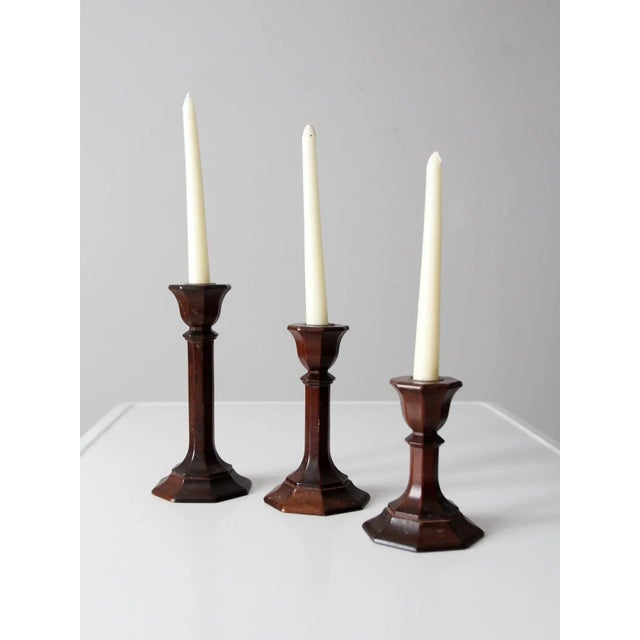 Set of three vintage wooden candlestick holders with turned column forms and brass sockets. Varying heights create an...