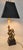 Late-20th-century brass-tone lion table lamp with a black hardback shade, reflective gold lining, and twin-leaf finial. It...