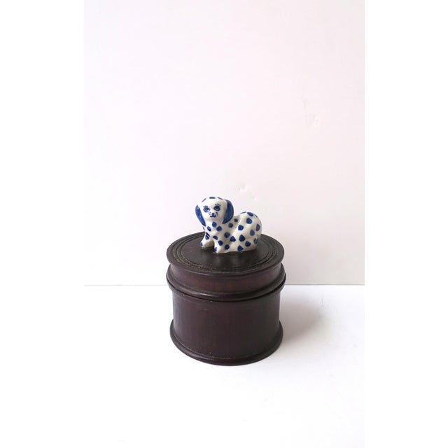 A rich dark brown teak trinket or jewelry box with a blue‑and‑white porcelain dog finial, circa mid‑20th century. A round...