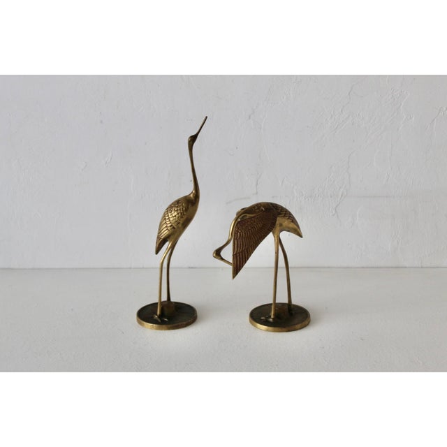 A pair of vintage mid-century modern brass crane sculptures with detailed feathering on the wings and a polished gold...