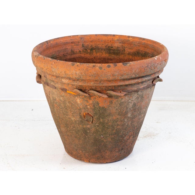 A large antique terracotta pot featuring a wide flared rim and a decorative rope twist detail encircling the upper body....