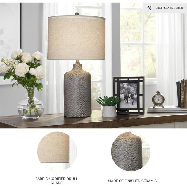 This contemporary ceramic table lamp features a sculptural white base with a smooth, glossy finish, paired with a soft...