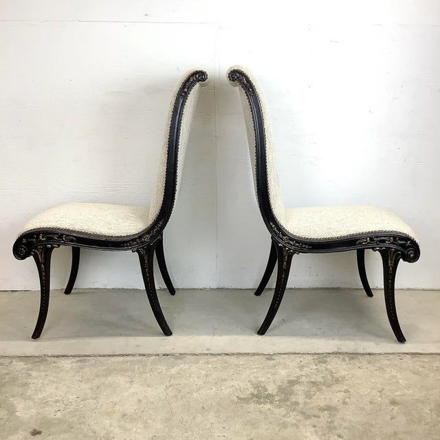 This stunning pair of high back regency modern slipper chairs feature ornate ebonized wooden frames with gilt detail and...