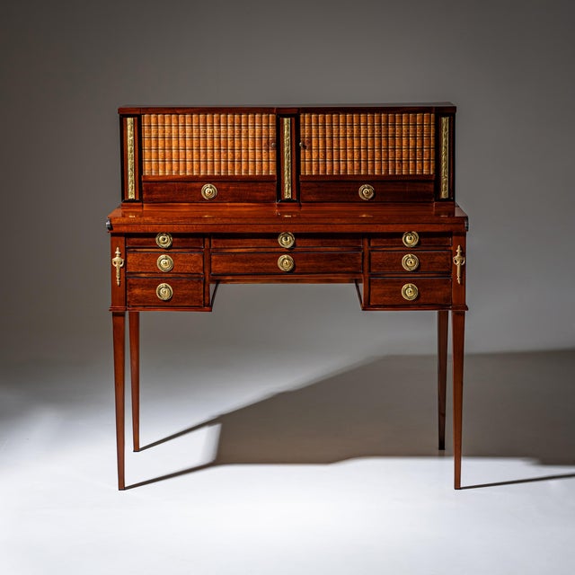 Desk veneered in mahogany with brass fittings and a total of eight drawers beneath the hinged writing top. When opened,...