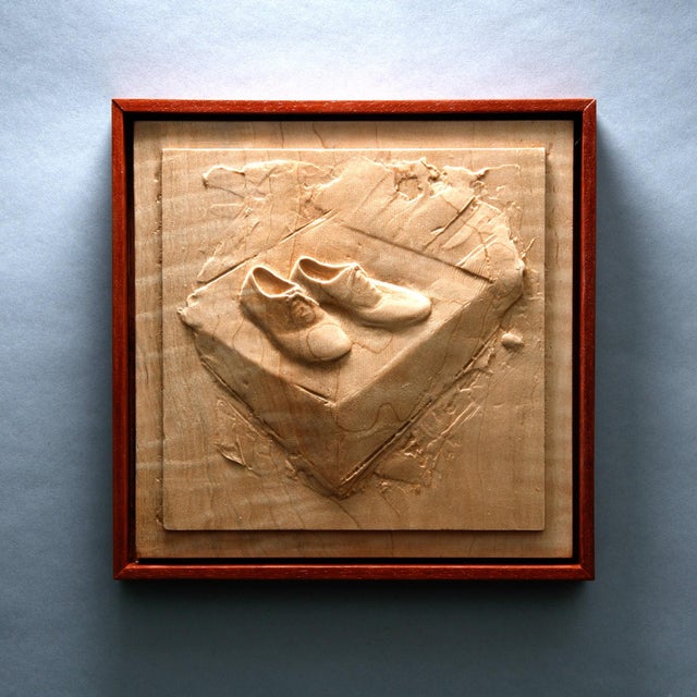 This artwork features a meticulously carved depiction of a pair of shoes resting atop a box, rendered in warm maple and...