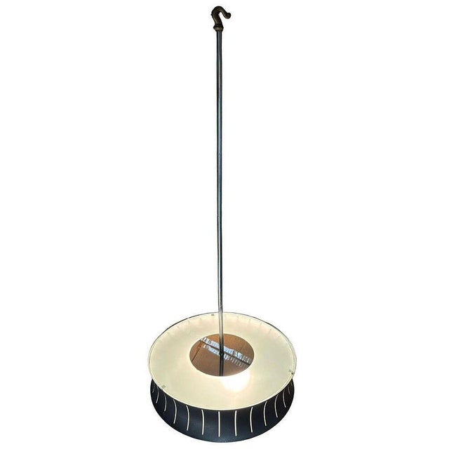 Mid-century Googie styled black drum pendant light with an interior white diffuser and a metal shade featuring vertical...