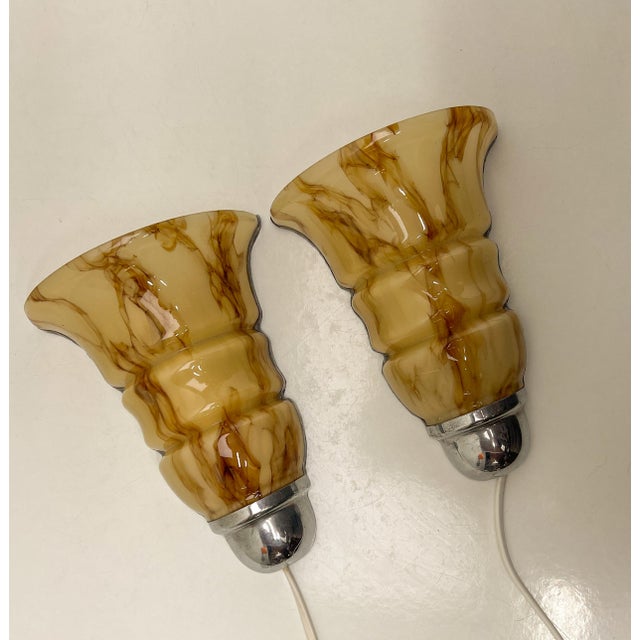 A set of Art Deco Style wall lamps made of glossy Acrylic with a nostalgic look. The shades have a marble pattern and a...