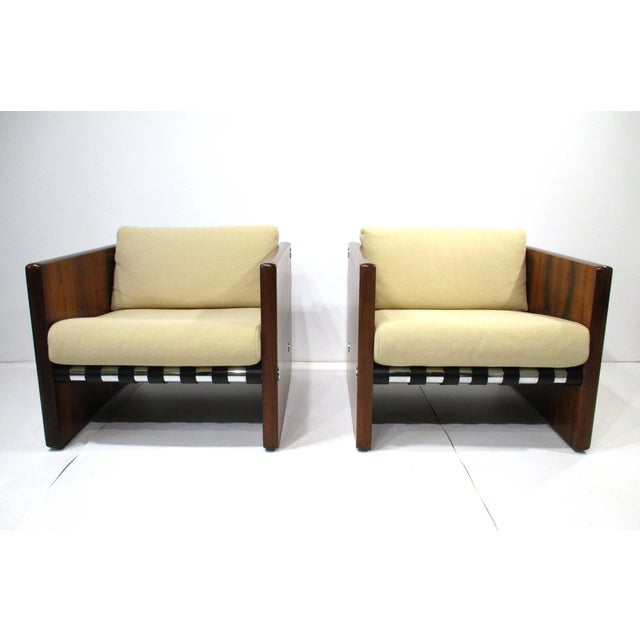 A pair of cubed club chairs with Brazilian rosewood slab sided legs, satin black leather straps and polished aluminum...