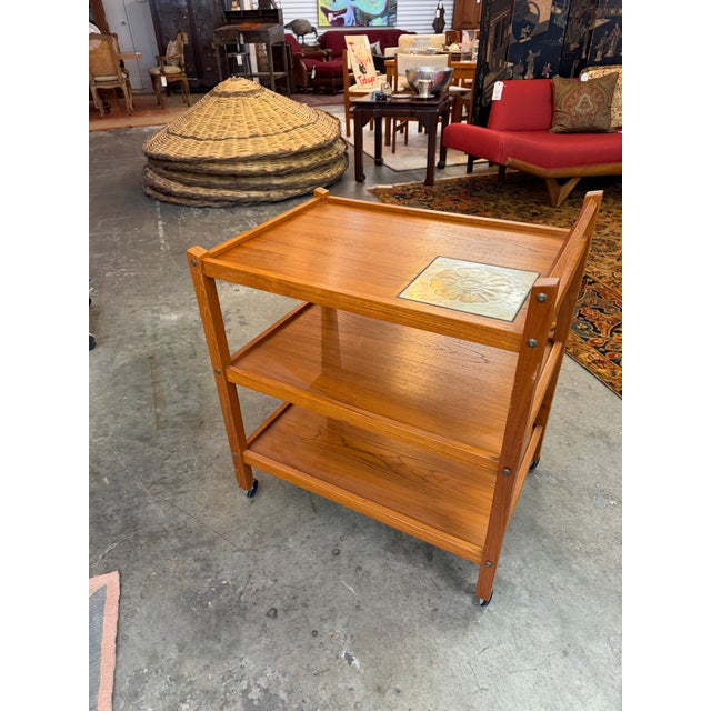 Constructed from richly grained teak with warm, glowing honey tones, the cart features a streamlined three-tier design...