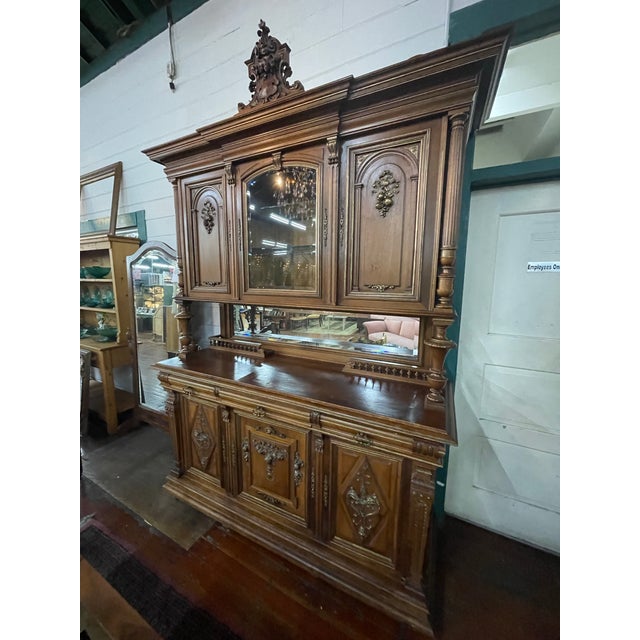 Features richly carved floral details, turned columns, paneled doors, and an ornate crown crest. The upper hutch w/...