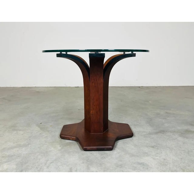 An elegant mid-century side table having bent walnut base under a 1/2” thick 24” diameter tempered glass top. Manufactured...