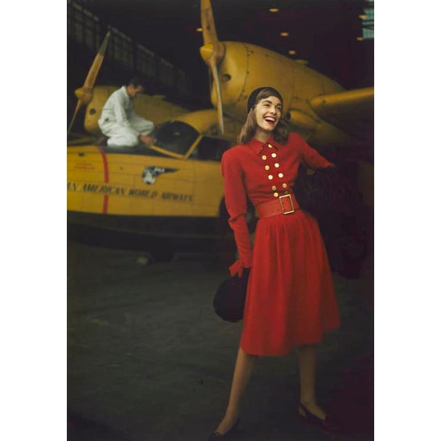 Model in a Red Dress 1959 A fashion shoot featuring a model in a red dress in front of a yellow aeroplane. Toni Frissell...