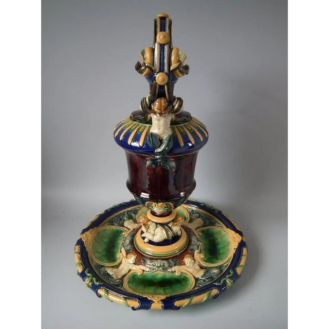 Minton Majolica ewer and stand which features putti supporting the stem of the ewer, a cherub riding a dolphin below the...