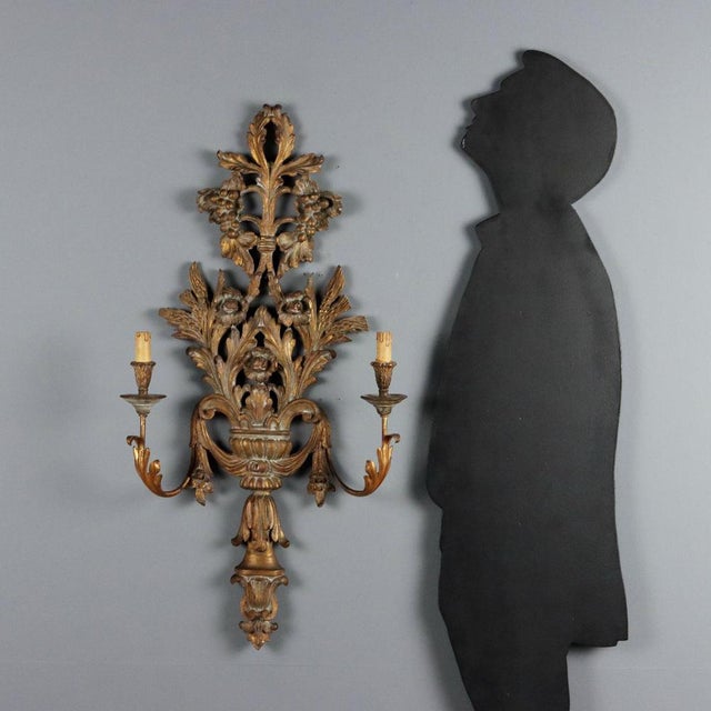 Carved and gilded wood wall sconce. Two lights supported by iron and sheet metal arms decorated with leaves, perforated...