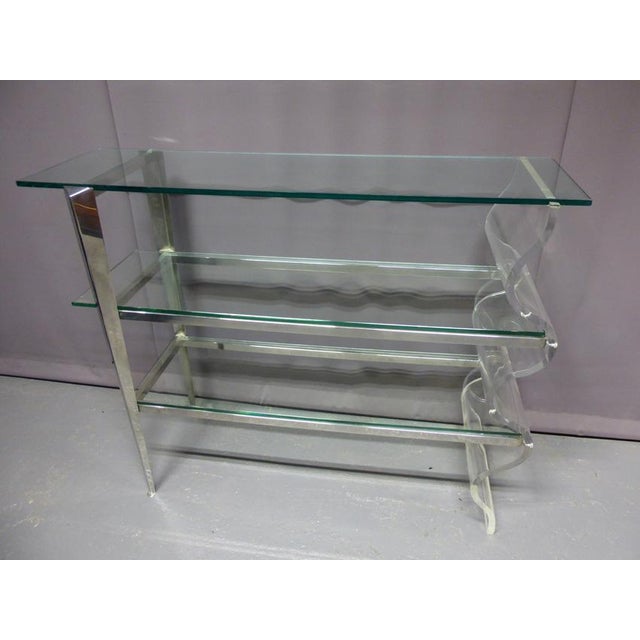 Large console shelf, metal structure, a side in acrylic glass of undulated form and three glass trays. This piece of...