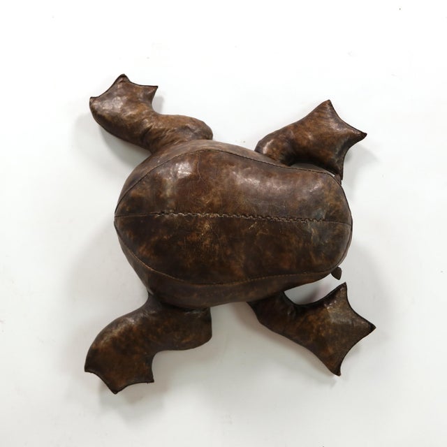 A low frog-form footstool in mottled brown leather, the rounded body formed from shaped stitched panels with a long hand-...