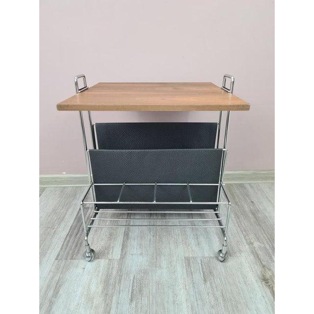 An elegant, mobile side table with a magazine rack, designed in the modernist style characteristic of the 1970s. The...