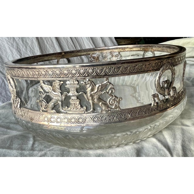 This is a clear glass bowl that is decorated in silver with alternating images of a laurel wreath with a long bow,...