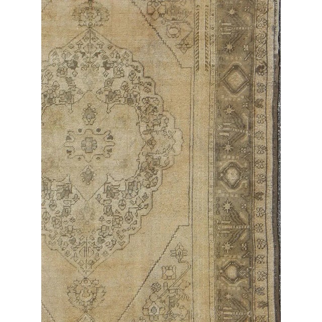 Measures: 5'7 x 9'7 This beautifully muted antique Turkish Oushak displays a stretched central medallion filled with Sub-...
