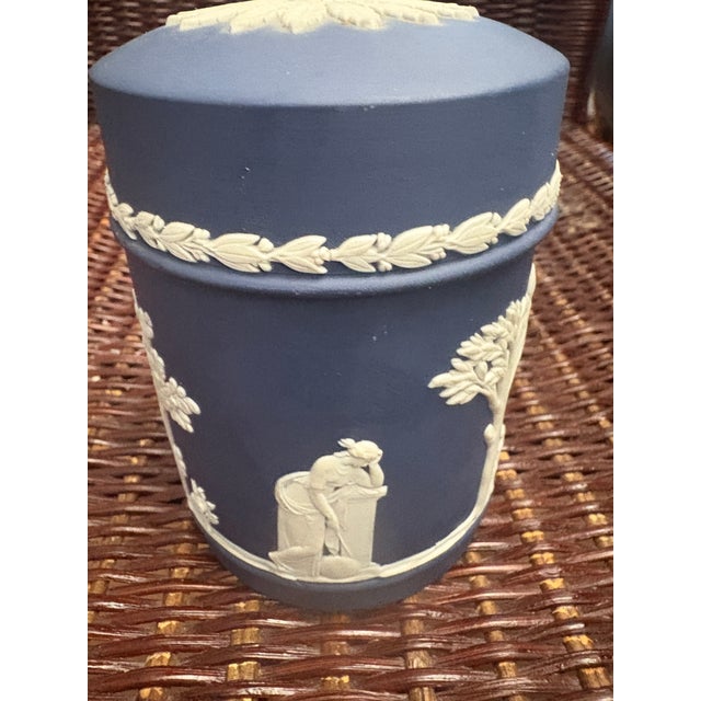 This is a Wedgwood Portland Blue Jasperware cylindrical lidded box featuring classic white neo-classical bas-relief...