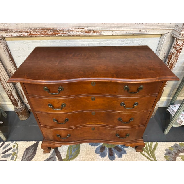 This is a 20th century vintage Eldred Wheeler serpentine chest of drawers. It is cherry wood. It has an ogee bracket base....