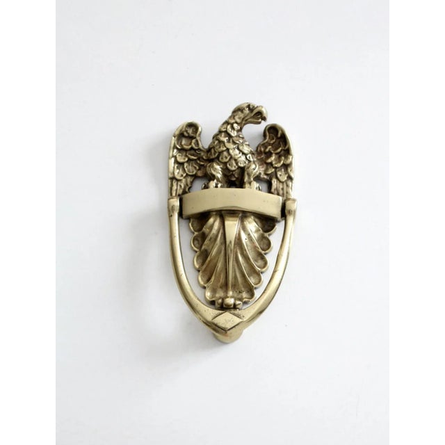 This is a vintage brass door knocker. Shaped as an American eagle perched atop a crest with swinging handle knocker....