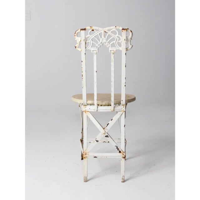 Antique white iron garden chair with a heavy, weighted frame. Features an art deco-inspired backrest and leg accents, and...