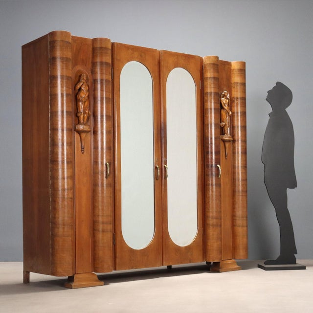 Wardrobe with hinged doors in walnut veneer, features decorative carved wood sculptures, with a female subject, mirrored...