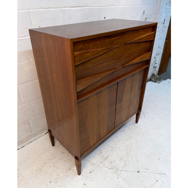 A striking Mid-Century Modern highboy dresser featuring rich walnut tones, beautifully figured wood grain, and distinctive...