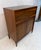 A striking Mid-Century Modern highboy dresser featuring rich walnut tones, beautifully figured wood grain, and distinctive...
